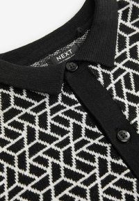 Schwarz-weißer Cardigan mit geometrischem Muster, Knopfblende und schwarzem geripptem Kragen. Strukturiertes Strickgewebe.
