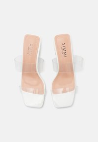 Mule-uri deschise, din piele patent albă, cu curele din PVC transparent și branț într-o nuanță nud. Prezintă un vârf pătrat și un design cu toc mic și gros.