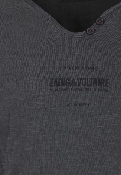 T-shirt gris foncé avec un décolleté en V, texture côtelée, deux accents de bouton et texte imprimé. Présente des rayures horizontales légères.