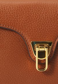 Borsa in pelle marrone con texture, dotata di una fibbia triangolare oro e un gancio prominente. La cucitura a contrasto delineano il pattina.