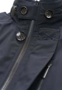 Marineblaue Jacke mit hoch geschlossenem Kragen, schwarzen Knöpfen und einem zentralen Reißverschluss mit strukturierter Oberfläche. Enthält eine Tasche mit elegantem Design.