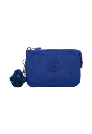 Pequeño bolso rectangular de tela azul con cremallera y parche redondo con logotipo, con un llavero de gorila de peluche azul adjunto.