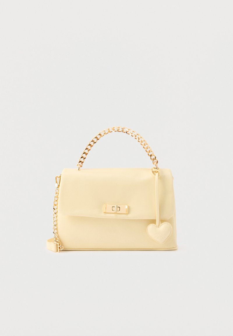 Sac à main couleur crème avec anse chaîne dorée, fermoir avant et pendentif en forme de cœur suspendu sur le côté.