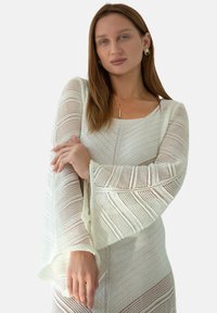 Jasna, dziana sweterek wykonany z lekkiego materiału, z szerokim dekoltem, rozkloszowanymi rękawami oraz teksturowanym wzorem w zygzak.