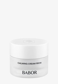 Heldere glazen pot met een gladde, ronde vorm. Witte deksel heeft een minimalistisch logo. Etiket zegt "Calming Cream Rich" in vette zwarte lettertype.