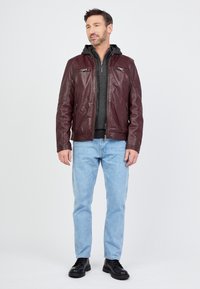 Burgunderlederjacke mit zwei vorderen Reißverschluss-Taschen, getragen über einem grauen Hoodie, kombiniert mit blauen Jeans und schwarzen Schuhen.