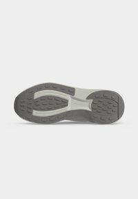 Semelle d'une chaussure de sport grise et blanche avec des motifs de bande de roulement texturés sur un fond blanc uni.