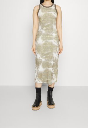 Ærmeløs midi-kjole med beige og hvid tie-dye-mønster og svag gul skrift, båret med sorte sokker og chunky sorte støvler med lysebrune såler.