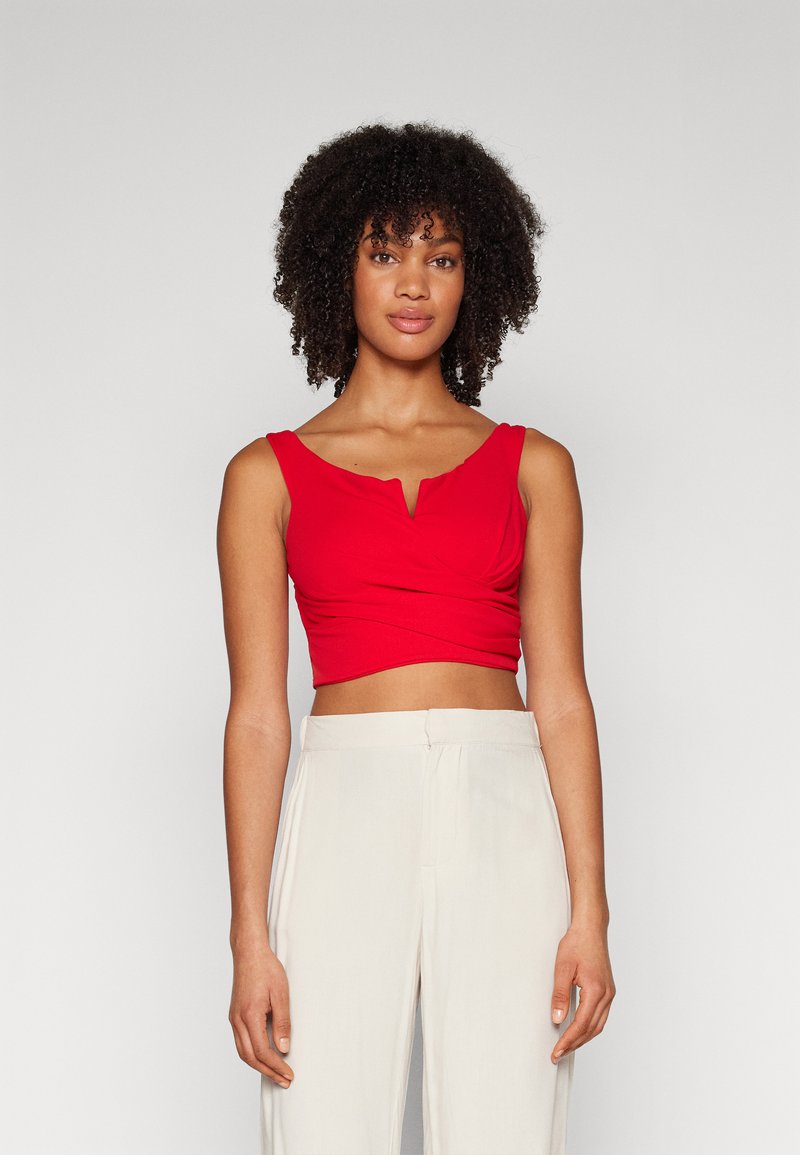 Top corto rosso con scollatura a V e design frontale annodato, realizzato in un tessuto liscio. Abbinato a pantaloni a vita alta di colore chiaro.