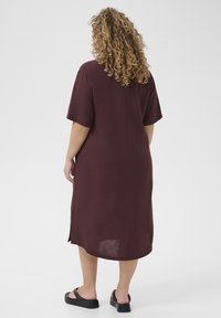 Burgundy short-sleeve dress made of lightweight fabric, featuring a relaxed fit, side slits, and a below-the-knee length. Worn with black sandals.