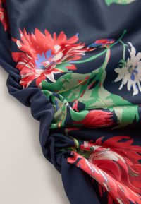 Tissu floral avec des motifs rouges, bleus et verts sur un fond bleu marine, présentant une texture froncée sur un bord. Matière douce et fluide.