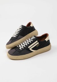 Sneaker neri e grigi con lacci bianchi, tessuto testurizzato e suole in gomma, con un accento crema e dettagli del logo sul lato.