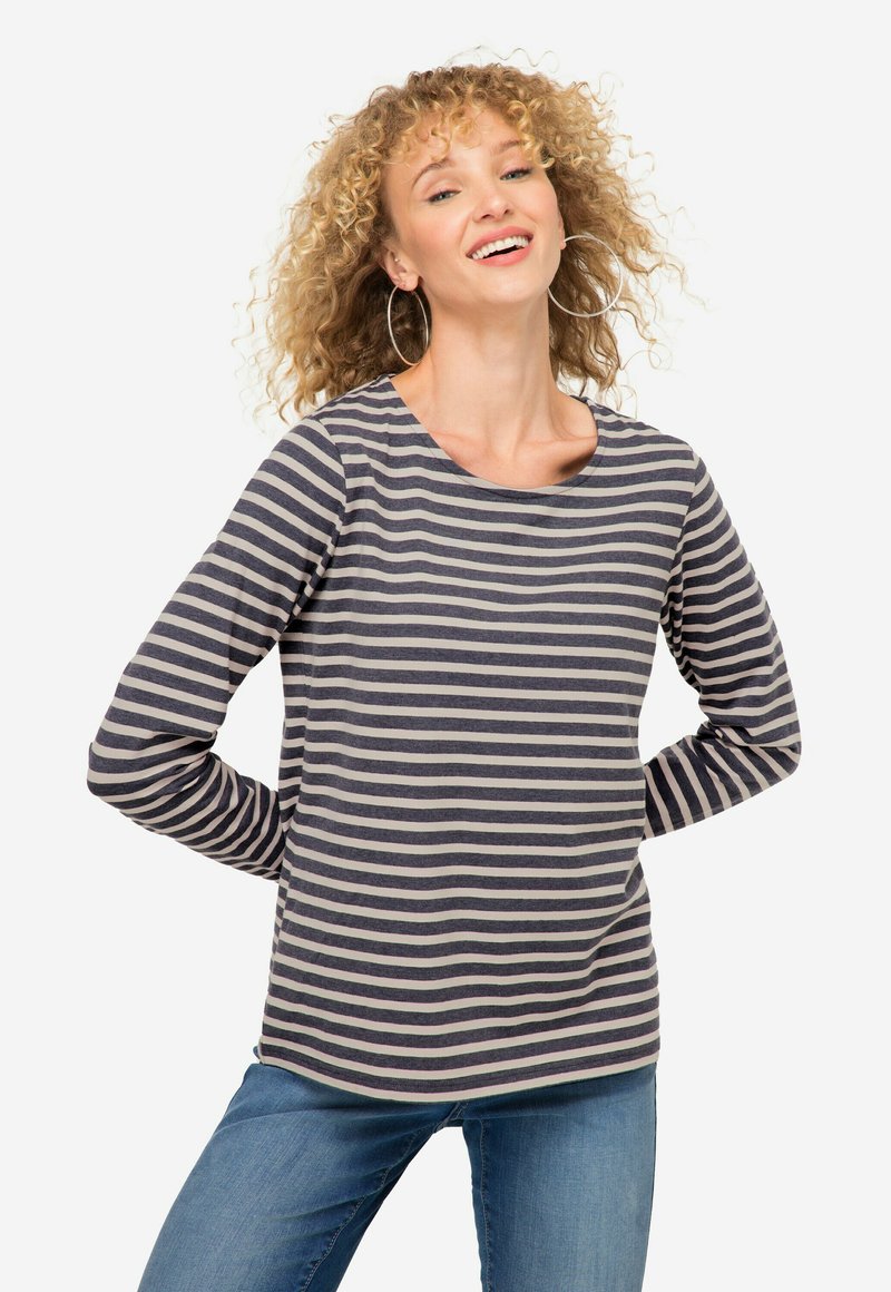 Chemise rayée à manches longues en bleu marine et beige. Mélange de coton doux avec un col rond et un ourlet arrondi. Portée avec un jean bleu clair.