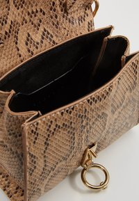 Handväska med pytonmönster i beige, med en strukturerad design, svart innerfoder och ett guldfärgat hårdvaruaccent med en ring.