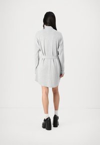 Vestido cinza de malha com mangas longas, cintura com cinto e barra arredondada. Usado com sapatos plataforma pretos e meias brancas.