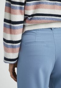 Pull en tricot rayé de couleur blanche, rose, bleue et marine. Texture douce associée à un pantalon léger bleu clair avec une poche au dos.