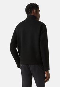 Sort jakke med høj krave, lavet af tekstureret stof. Har et enkelt design, afslappet pasform og sidelommer.