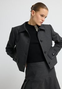 Szary dopasowany żakiet z czarnym skórzanym kołnierzem, z dużymi guzikami i delikatnym prążkiem. Nosi się go na czarnym swetrze z prążkowanej dzianiny z perłowym akcentem.