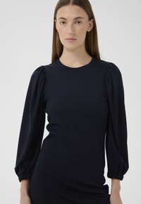 Rochie albastru marin cu mâneci bufante structurate, decolteu rotund și textură fină. Siluetă cambrată cu detalii adunate la manșetele mânecilor.