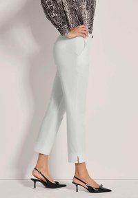 Lichtgrijze op maat gemaakte broek met een slim fit, voorzien van zijzakken en gespleten uiteinden, gecombineerd met zwarte slingback hakken met puntige neuzen.
