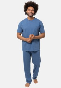 Sininen puuvillapuvun setti, jossa on lyhythihainen paita, jossa on tasku, ja väljästi istuvat housut. Pehmeä textura, rento leikkaus ja yksinkertainen muotoilu.