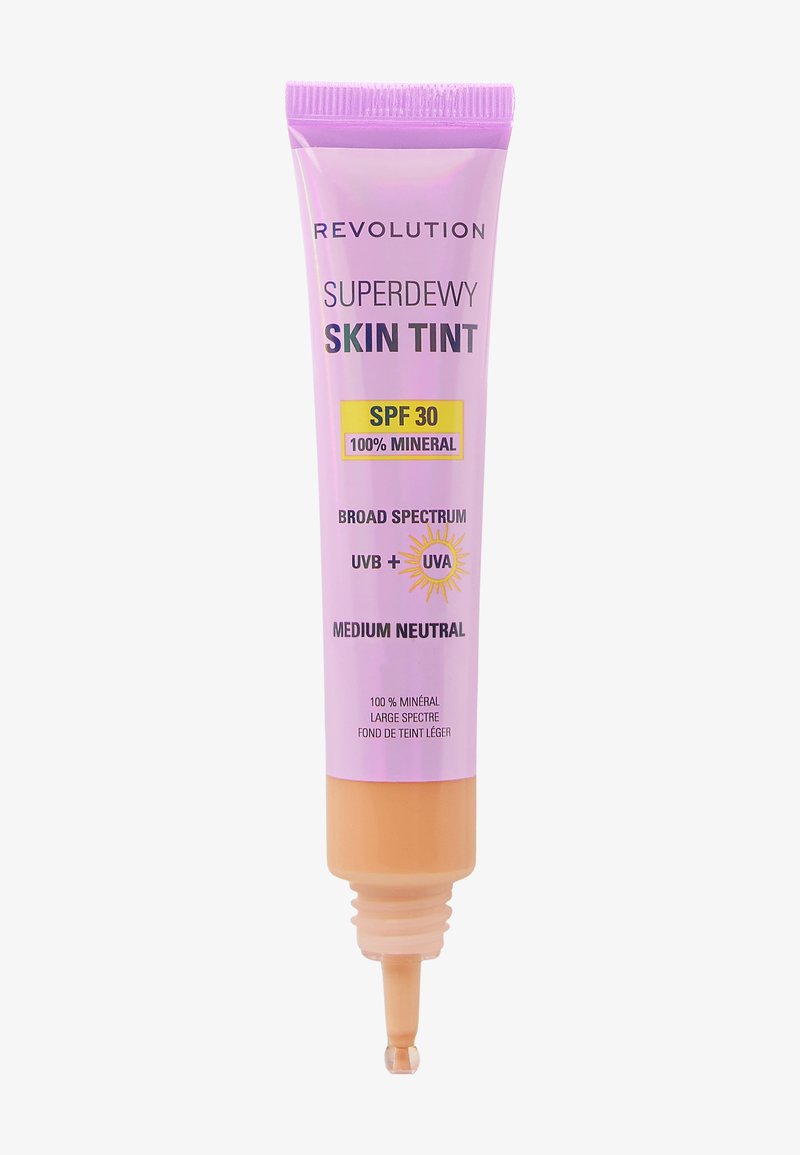 Superdewy Skin Tint de Revolution dans un tube violet avec un bouchon beige. L'étiquette indique SPF 30, 100 % minéral, et une teinte moyenne neutre.