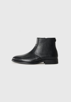 Bota de tobillo negra de cuero con punta redonda, textura suave, tacón bajo y detalle de cremallera lateral para facilitar su uso.