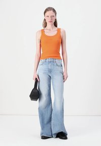Top naranja de canalé, jeans flare de cintura alta en azul claro y bolso negro. La modelo se encuentra de pie con las manos a los lados sobre un fondo liso.