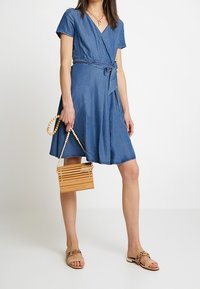 Denim-vuori mekko, jossa on lyhyet hihat, V-pääntie ja vyötäröllä solmittu vyö. Yhdistetty puiseen, raidalliseen käsilaukkuun ja vaaleisiin sandaaleihin.