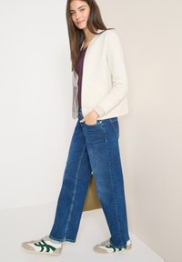 Světlé šedé pruhované zipové sáčko se šedou podšívkou, kombinované s tmavě modrými širokými džíny a šedými teniskami se zelenými pruhy.