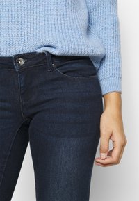 Donkere denim jeans met een gladde textuur, voorzien van een metalen knoopsluiting, riemlussen en een klassieke vijf-pocket ontwerpen.