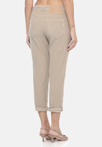 Pantaloni beige a vita alta con orli arrotolati e tasche posteriori indossati da una persona che sta in piedi a piedi nudi su uno sfondo bianco.
