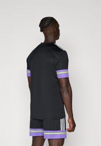 Zwarte sportshirt met paarse en groene gestreepte accenten op de mouwen, gecombineerd met zwarte shorts met vergelijkbare gestreepte details.