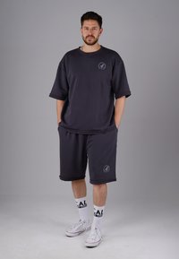 Dunkelgrauer, übergroßer Sweatshirt und passende Shorts, beide aus einem weichen Stoff, mit einem Logo-Detail und lockerer Passform. Weiße Socken und Sneakers.