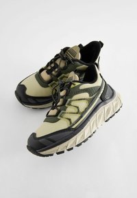 Szczotkowane sneakersy w beżowym i oliwkowym kolorze z siateczkowymi i gumowymi materiałami, teksturowanymi akcentami, masywną podeszwą oraz kontrastującymi czarnymi detalami.