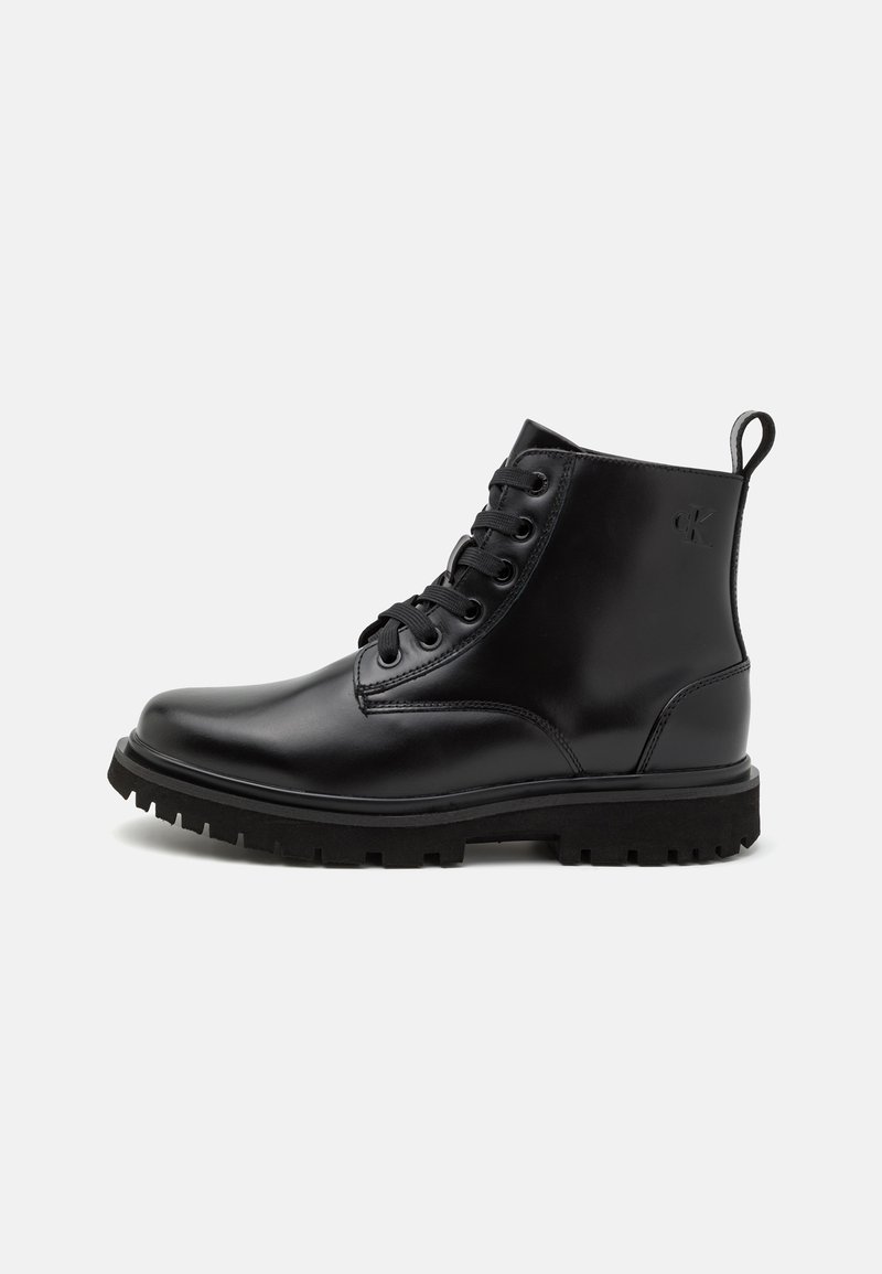 Botas de tobillo de cuero negro con diseño de cordones, puntera redonda y suela de goma resistente. Presenta un detalle del logotipo en el lado exterior.
