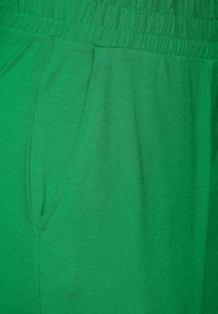 Shorts en coton verts avec une taille élastique et des poches latérales, présentant une texture lisse et un design simple sans motifs.