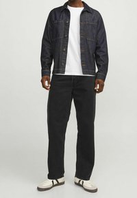 Chaqueta de mezclilla oscura con botones, combinada con una camiseta blanca y jeans negros ajustados. Zapatillas beige con detalles negros.