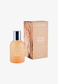 Transparent glasflaska med ett metalliskt silverlock, innehållande en ljus orange vätska. Förpackningen har ett träfibrigt mönster och beige bakgrund.