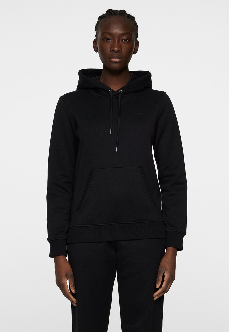 Svart huvtröja i mjukt material, med en framficka, ribbade ärmslut och en subtil logga på bröstet. Enkelt design.