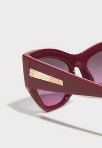 Vogue saulės akiniai su tamsiai bordo plastiko rėmeliu, geometrine katės akies forma, gradientinėmis violetinėmis lęšiais ir auksinės spalvos logotipo detalėmis.