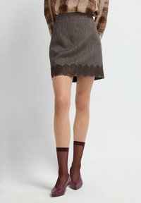 Mini gonna marrone con texture e bordo in pizzo, abbinata a calze trasparenti color bordeaux e scarpe a taglio basso abbinate.