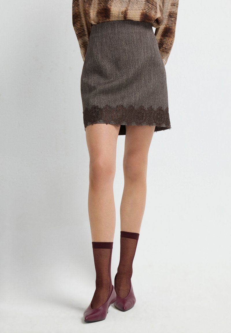 Mini gonna marrone con texture e bordo in pizzo, abbinata a calze trasparenti color bordeaux e scarpe a taglio basso abbinate.