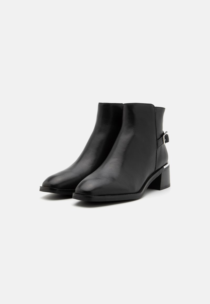 Botas de cuero negras hasta el tobillo con punta afilada, tacón bajo en bloque y una correa lateral con detalles en hardware plateado. Textura suave, diseño elegante.