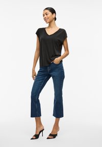 Črna kratka majica z V-izrezom, kombinirana s temno moderimi skrajšanimi jeans hlačami in črnimi odprtimi mule sandali z visokimi petami. Gladek material z udobnim krojem.