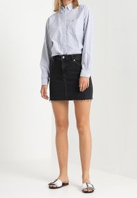 Camicetta a righe blu e bianche con maniche lunghe, gonna di jeans neri con orlo sfilacciato e sandali bianchi con dettagli neri.