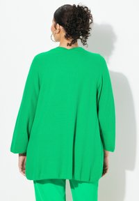 Överdimensionerad grön stickad topp med en texturerad yta, lösa trekvartslånga ärmar och V-ringning. Har sidslitsar och en avslappnad passform.