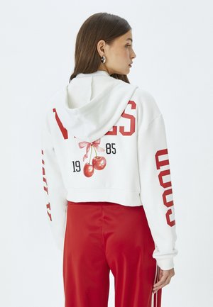 Korte witte hoodie met rode tekst, voorzien van een kersengrafiek en strik. De stof lijkt zacht en glad, met een trekkoord capuchon.