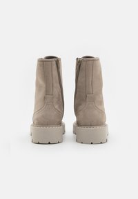 Beige mokkasino nilkkurit, joissa on sileä pinta, sivuvetoketjut ja paksu, chunky-tyylinen kermavärinen pohja, jossa on sahalaitaiset reunat.