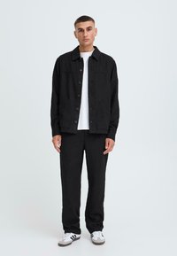 Zwarte jas met een knoopsluiting aan de voorkant, twee zijzakken, gecombineerd met bijpassende zwarte broek en een wit T-shirt, met witte en grijze sneakers.